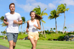 Leg Pain Relief: People running in city park. Happy young couple living an active healthy lifestyle jogging training their cardio during summer on road or neighborhood street. Multiracial group, Asian and Caucasian.