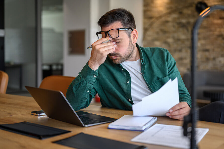 Stress and Spine Health. Anxious male financial advisor rubbing eyes while working over laptop and analyzing reports at desk